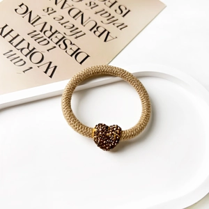 Close-up of khaki woven hair tie featuring a sparkling coffee-colored rhinestone heart