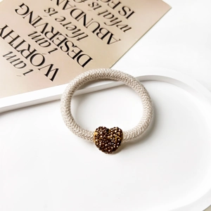 Detail of beige knit elastic hair tie featuring a sparkling gold rhinestone heart pendant