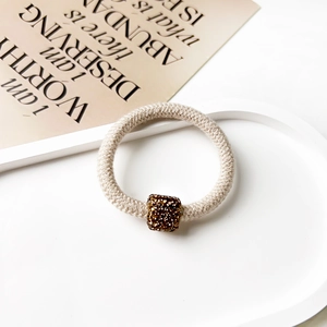 Detail of beige knitted hair scrunchie with a square brown rhinestone bead on white base