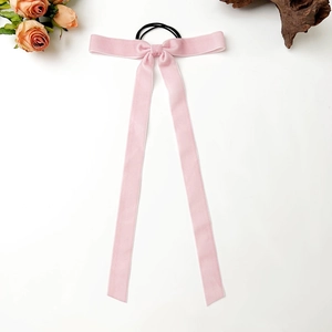 Close-up of pink velvet bow hair scrunchie with long ribbons on white surface