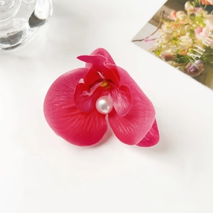 Close-up of elegant magenta orchid hair clip with pearl center and floral card backdrop