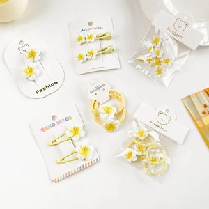 Flat lay of yellow frangipani hair clips and floral scrunchies on white paper cards