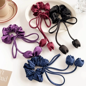 Detailed view of four satin tulip ribbon hair scrunchies on an elegant tea table setting