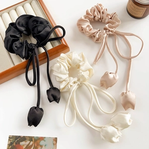 Detailed view of three satin scrunchies with long ribbons and tulip flower charms