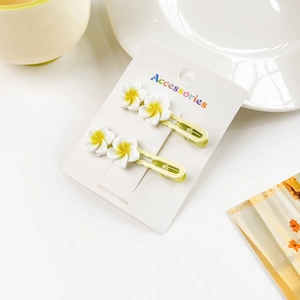 Close-up of two frangipani hair clips on a card with soft warm minimalist lighting