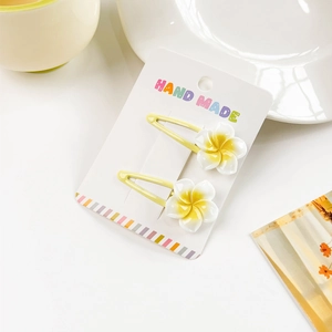Detail of yellow handmade plumeria hair clips with white resin petals on paper card