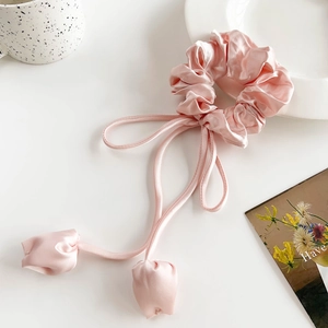 Detailed macro view of pink satin tulip scrunchie with long ribbons on white surface