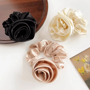 Detail of elegant satin rose scrunchies in black, cream, and champagne gold