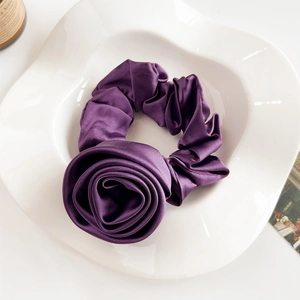 Close-up of deep purple satin rose scrunchie with silky luster on a ceramic plate
