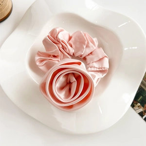 Detailed close-up of a pink satin rose hair tie on a white ceramic plate