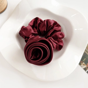 Macro detail of wine red satin scrunchie styled as a rose on a decorative ceramic plate