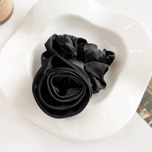Detail of a black satin rose scrunchie on a white ceramic tray with elegant textures