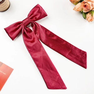 Detail einer burgunderroten Satin-Haarschleife mit langen Bändern auf weißem Grund