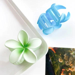 Close-up of matte plumeria flower hair claws in gradient green and light blue colors