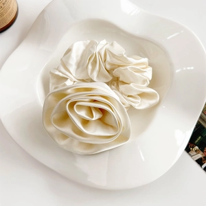 Detailed view of elegant cream white satin rose scrunchie on a white ceramic plate