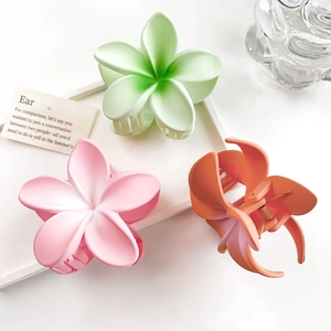 Three matte plumeria flower hair claws in green, pink, and orange on a white tray