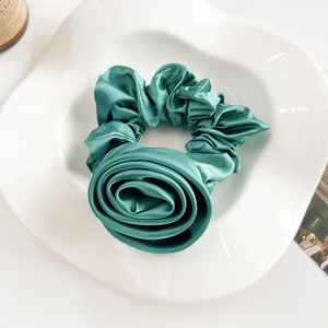 Detail of elegant dark green satin rose hair tie on a white ceramic display plate