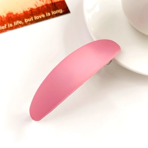 Détail de la barrette à cheveux rose mat en forme de croissant montrant sa texture et son ressort