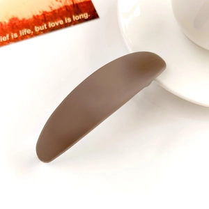 Détail de la pince à cheveux ovale marron mat avec texture givrée sur table blanche
