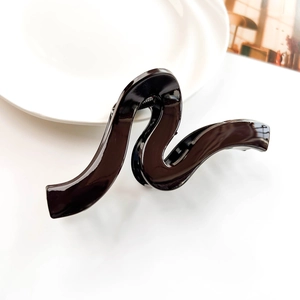 Close-up of black glossy geometric wave hair claw clip on white decorative background