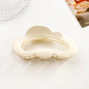 Detail of a matte cream cloud-shaped hair claw clip on a minimalist white background