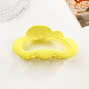 Detail of matte yellow cloud-shaped hair claw clip with frosted texture and wavy design