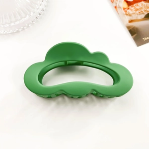 Detail showing the matte grass green cloud-shaped hair claw clip on a white surface