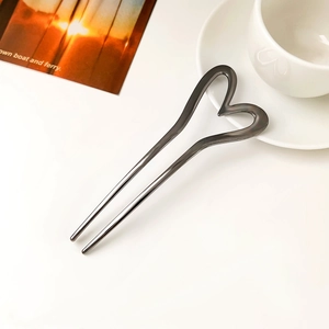 Detail of gun-black U-shaped metal hair pin with heart top on a white desk
