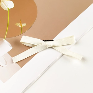 Detailed view of a creamy white ribbon bow hair clip with a minimalist textured fabric design