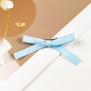 Macro detail of the light blue silk ribbon bow hair clip with black metal duckbill clip