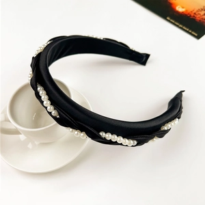 Detail of elegant black braided headband with white pearls and smooth satin texture