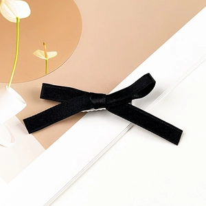 Close-up of elegant black grosgrain ribbon bow hair clip on minimalist cream background