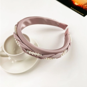 Close-up of pink satin braided headband with delicate pearl accents on ceramic saucer