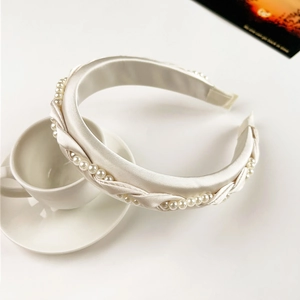 Detail of cream satin braided headband with white imitation pearls on a white cup