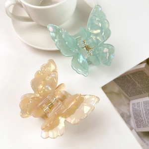 Detail view of iridescent 3D butterfly hair claws in mint green and peach pink tones