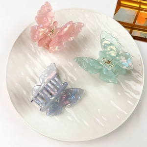 Detailed view of three iridescent butterfly hair clips in pink, green and blue shades
