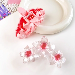 Dettaglio mollette per capelli a forma di fiori con sfumature rosa e rosse su piatto bianco