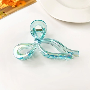 Detail of iridescent blue bow hair claw clip showing glossy pearl finish and metal spring