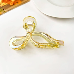 Close-up of translucent yellow bow claw clip with iridescent finish and metal spring
