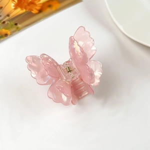 Detailed close-up of a pink iridescent butterfly hair claw clip with golden metal spring
