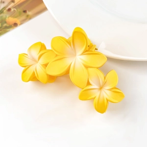 Vista dettagliata di tre fiori di frangipani gialli su una pinza per capelli opaca