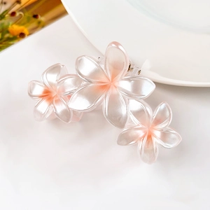 Dettaglio della molletta per capelli con fiori di plumeria sfumati rosa e perlescenti