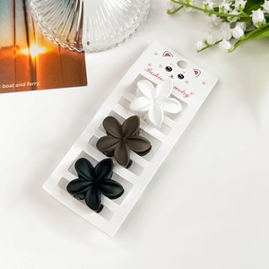 Détail de trois pinces à cheveux fleurs mates en blanc, marron et noir sur support