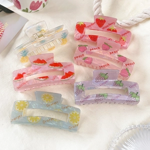 Flat lay of colorful semi-transparent PVC fruit hair claws on white linen fabric background