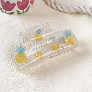 Detail of pearlescent white hair claw clip with yellow pineapple patterns and text