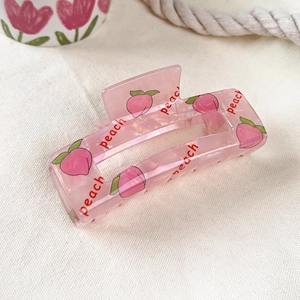 Detailed macro view of a peach-patterned pink PVC hair claw clip on a soft white texture