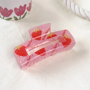 Detailed close-up of a pink PVC strawberry hair claw clip on a white textured fabric