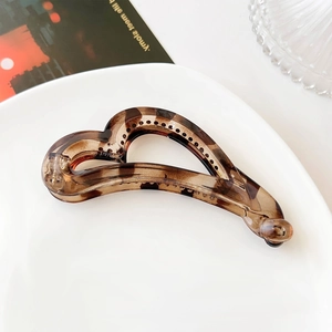 Detail of dark brown tortoiseshell heart banana clip on a white ceramic tray
