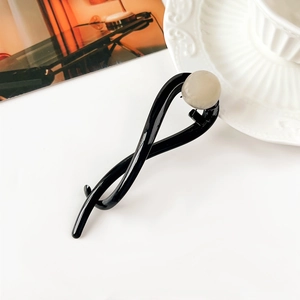 Dettaglio di un fermaglio per capelli nero intrecciato con finitura lucida e perla color crema
