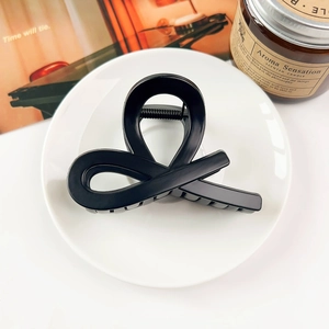 Detail of a minimalist black twist hair claw clip on a white ceramic tray with accessories